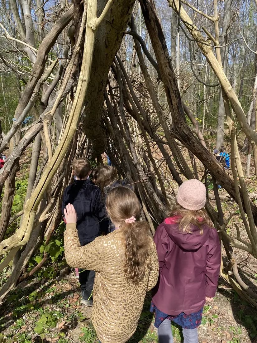 Zwei Kinder stehen vor einer selbst gebauten Hütte aus Ästen und Zweigen.