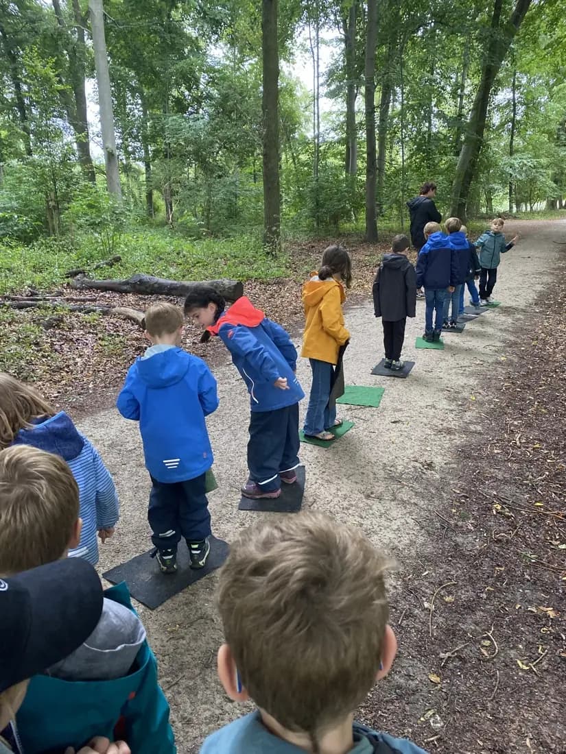 Eine Schulklasse geht auf einem Waldweg hintereinander her, vorne bücken sich mehrere Kinder zu etwas am Boden.